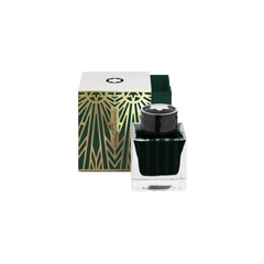 Um frasco de tinta Montblanc com uma tampa preta e a metade inferior transparente preenchida com tinta verde escura está colocado em frente à sua embalagem. A caixa é branca com um padrão geométrico verde e dourado e o logotipo da Montblanc no topo. O design sugere elegância e luxo, típicos da marca Montblanc