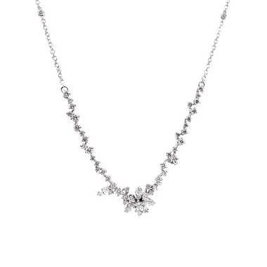 Um delicado colar de ouro branco apresentando um design simétrico com uma corrente de pequenos diamantes redondos que levam a um ponto central onde diamantes maiores estão dispostos em um aglomerado semelhante a uma flor. O colar tem uma aparência elegante e luxuosa, com os diamantes cintilando contra o cenário de ouro branco.