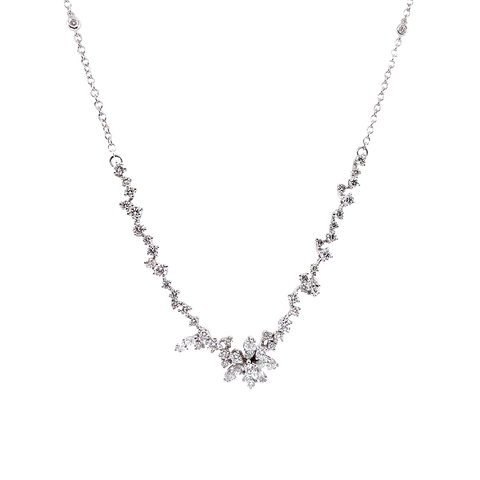 Um delicado colar de ouro branco apresentando um design simétrico com uma corrente de pequenos diamantes redondos que levam a um ponto central onde diamantes maiores estão dispostos em um aglomerado semelhante a uma flor. O colar tem uma aparência elegante e luxuosa, com os diamantes cintilando contra o cenário de ouro branco.