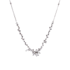 Um delicado colar de ouro branco apresentando um design simétrico com uma corrente de pequenos diamantes redondos que levam a um ponto central onde diamantes maiores estão dispostos em um aglomerado semelhante a uma flor. O colar tem uma aparência elegante e luxuosa, com os diamantes cintilando contra o cenário de ouro branco.