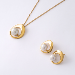 Colar de prata banhada a ouro com um pingente de pérola Murano, acompanhado por brincos combinando. Cada peça apresenta um exterior liso banhado a ouro que envolve elegantemente a pérola Murano branca e lustrosa, destacando-se contra um fundo branco limpo que realça a sofisticação e simplicidade das joias.