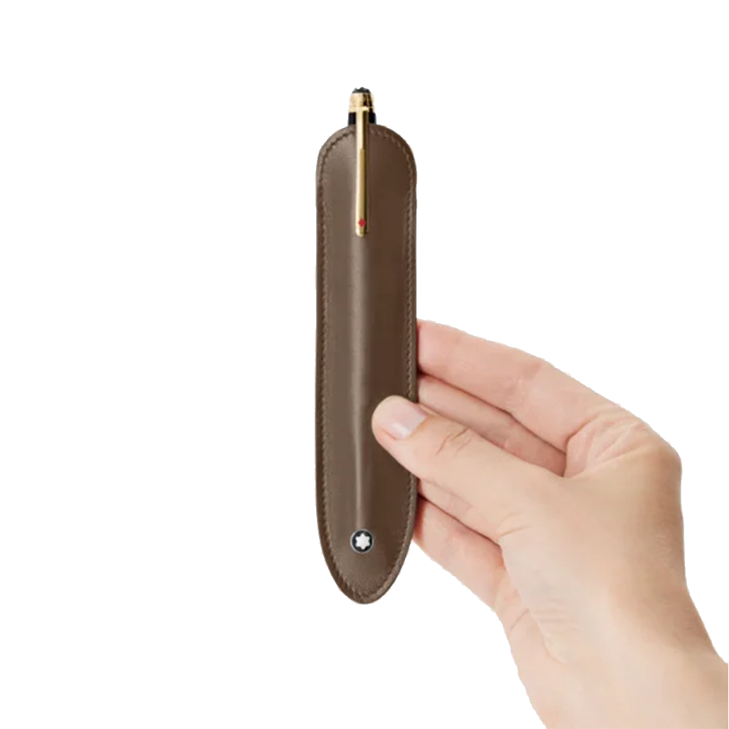 Uma mão segura uma elegante capa de caneta esferográfica castanha com detalhes dourados e um clipe, embainhada em um estojo de couro castanho com costura visível e fecho prateado