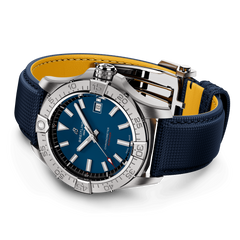Uma imagem de um relógio de pulso de luxo com um mostrador azul, detalhes em branco e prata, e uma janela de data na posição das 3 horas. O relógio tem uma moldura rotativa com números e marcadores, ponteiros luminosos e índices de horas. Está preso a uma pulseira de tecido azul com fundo amarelo, complementando o esquema de cores geral. O relógio está definido contra um fundo branco que destaca seus recursos de design.