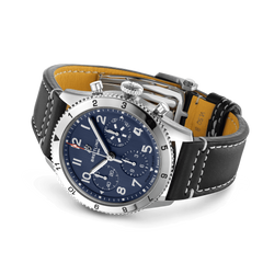 Relógio Breitling com mostrador azul, detalhes em branco e prata, três submostradores e janela de data na posição das 3 horas. A caixa é de aço inoxidável com aro giratório numerado. O relógio possui uma pulseira de couro bovino preta com costura branca e interior marrom claro.