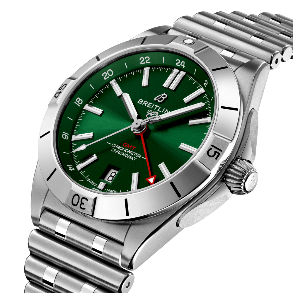 Relógio Breitling Chronomat de aço inoxidável com mostrador verde, marcadores e ponteiros prateados, janela de data às 6 horas e três submostradores. O bisel tem marcadores de minutos gravados e o relógio está preso a uma pulseira de aço inoxidável com fecho dobrável. A coroa e dois botões estão no lado direito da caixa.