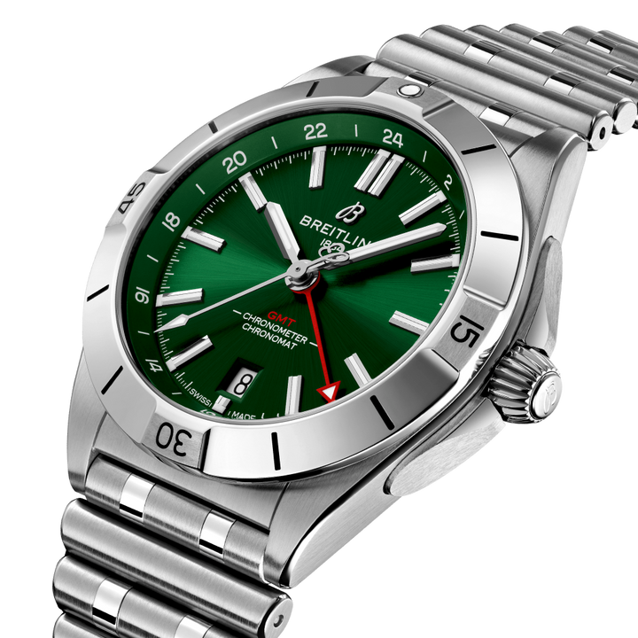 Relógio Breitling Chronomat de aço inoxidável com mostrador verde, marcadores e ponteiros prateados, janela de data às 6 horas e três submostradores. O bisel tem marcadores de minutos gravados e o relógio está preso a uma pulseira de aço inoxidável com fecho dobrável. A coroa e dois botões estão no lado direito da caixa.