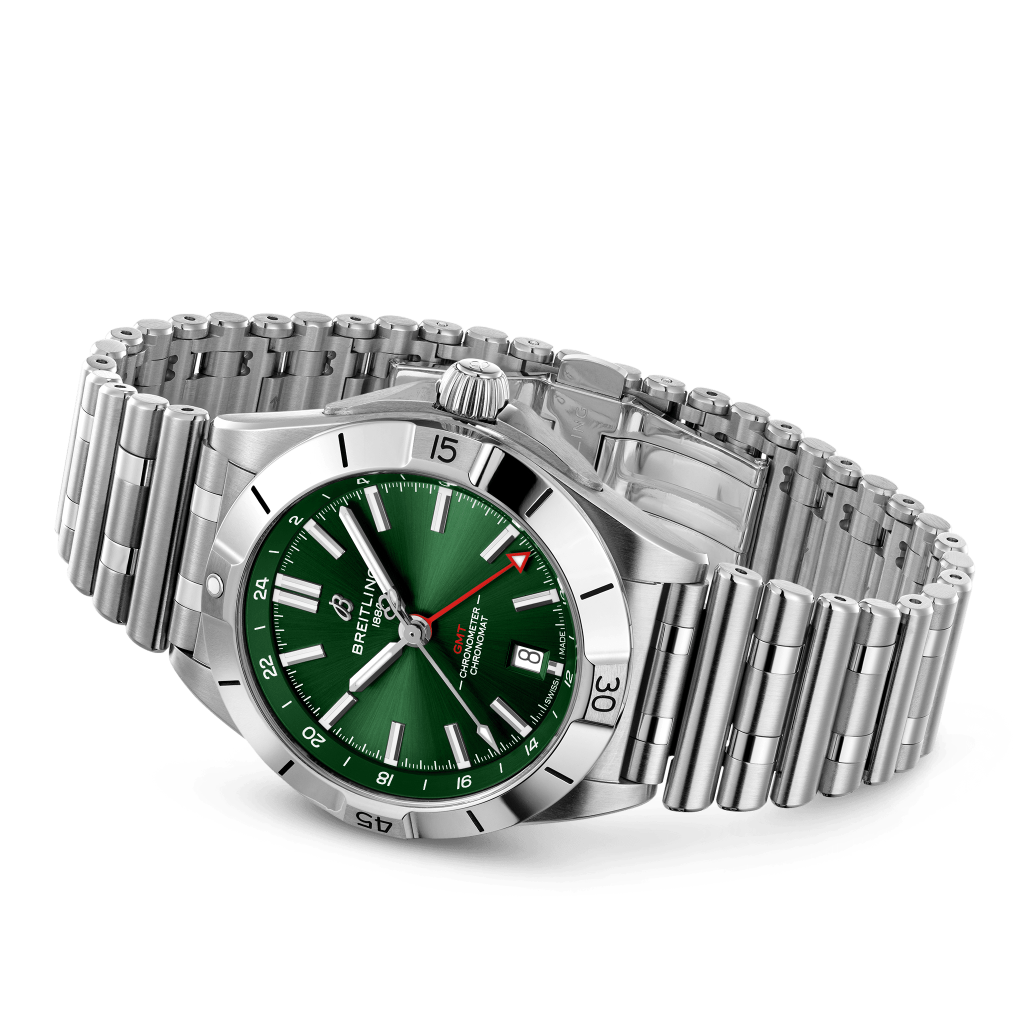 Relógio de pulso de aço inoxidável com mostrador verde vibrante, ponteiros e marcadores de horas luminosos. O relógio possui uma janela de data na posição das 3 horas, um bisel canelado e está preso a uma pulseira de elos com fecho dobrável. O nome da marca é visível na parte superior do mostrador.