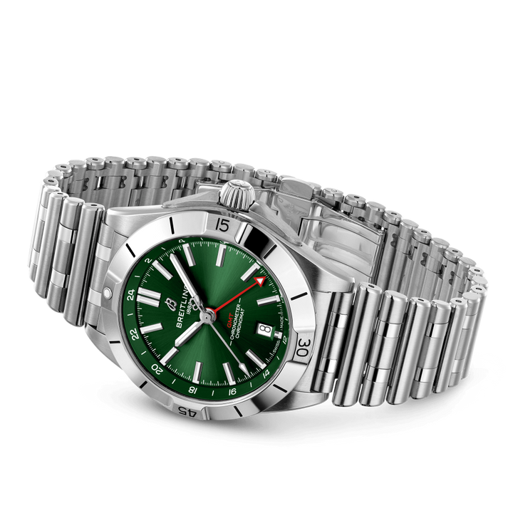 Relógio de pulso de aço inoxidável com mostrador verde vibrante, ponteiros e marcadores de horas luminosos. O relógio possui uma janela de data na posição das 3 horas, um bisel canelado e está preso a uma pulseira de elos com fecho dobrável. O nome da marca é visível na parte superior do mostrador.
