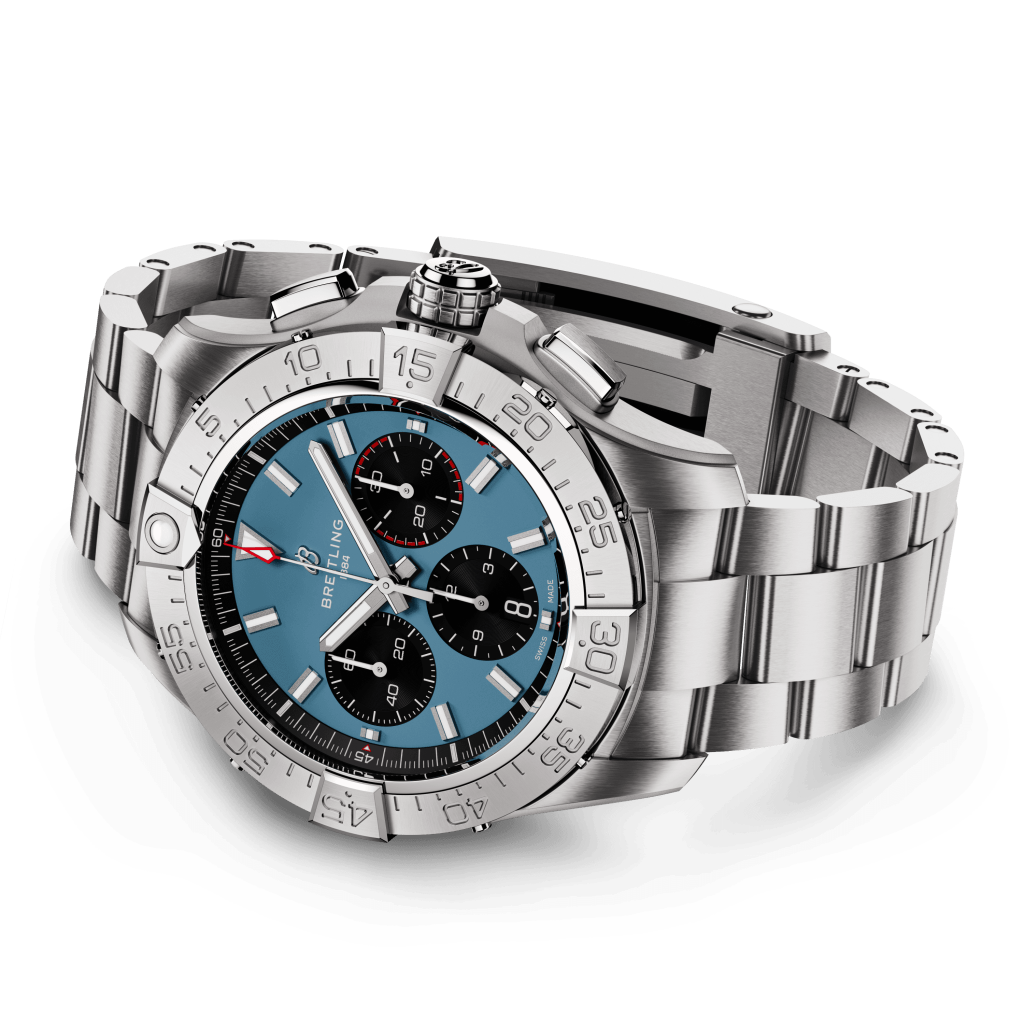 Um relógio de pulso de luxo com uma pulseira e caixa de aço inoxidável. O relógio apresenta um mostrador azul com três submostradores pretos, marcadores de hora e ponteiros em tom de prata, e um ponteiro de segundos vermelho. Há uma janela de data perto da posição das 3 horas, e a moldura tem marcadores de minutos gravados. A coroa e dois botões de pressão são visíveis no lado direito da caixa.