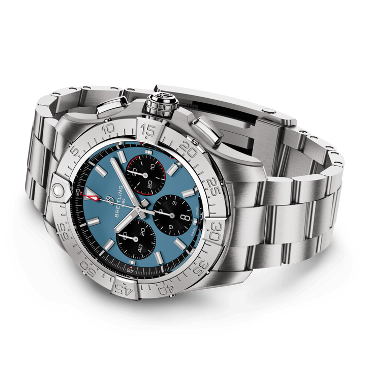 Um relógio de pulso de luxo com uma pulseira e caixa de aço inoxidável. O relógio apresenta um mostrador azul com três submostradores pretos, marcadores de hora e ponteiros em tom de prata, e um ponteiro de segundos vermelho. Há uma janela de data perto da posição das 3 horas, e a moldura tem marcadores de minutos gravados. A coroa e dois botões de pressão são visíveis no lado direito da caixa.