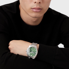 Relógio Emporio Armani de aço inoxidável com mostrador verde, ponteiros e marcadores de hora prateados, no pulso de uma pessoa vestindo uma manga preta