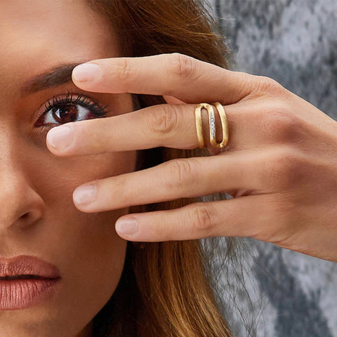 Senhora com o Anel NANIS Libera dourado em formato S com pequeno detalhe de diamantes no centro