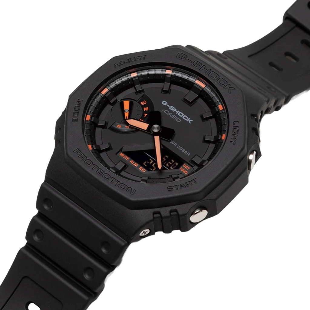 Um relógio de pulso G-Shock de resina preta com um mostrador digital-analógico. O mostrador apresenta acentos laranja e brancos nos ponteiros e marcadores de hora. A moldura ao redor do mostrador inclui etiquetas como ‘Adjust’, ‘Mode’, ‘Light’ e ‘Search’. Há também etiquetas para diferentes funções como ‘Shock Resist’ e ‘Water 20BAR Resist’. A pulseira é preta, combinando com o corpo do relógio, e parece ser feita de um material durável, adequado para uso ativo ou em ambientes rigorosos