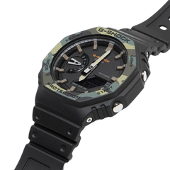 Relógio G-Shock de resina com pulseira preta, exibido contra um fundo branco. O mostrador é redondo e escuro, com detalhes em várias tonalidades de cinza e verde. Possui múltiplos mostradores e indicadores, incluindo um display digital na parte inferior. Os botões laterais são rotulados como ‘adjust’, ‘mode’, ‘light’ e ‘start/stop’ para facilitar diferentes funções. Esta imagem destaca o design e a funcionalidade de um relógio moderno e robusto.