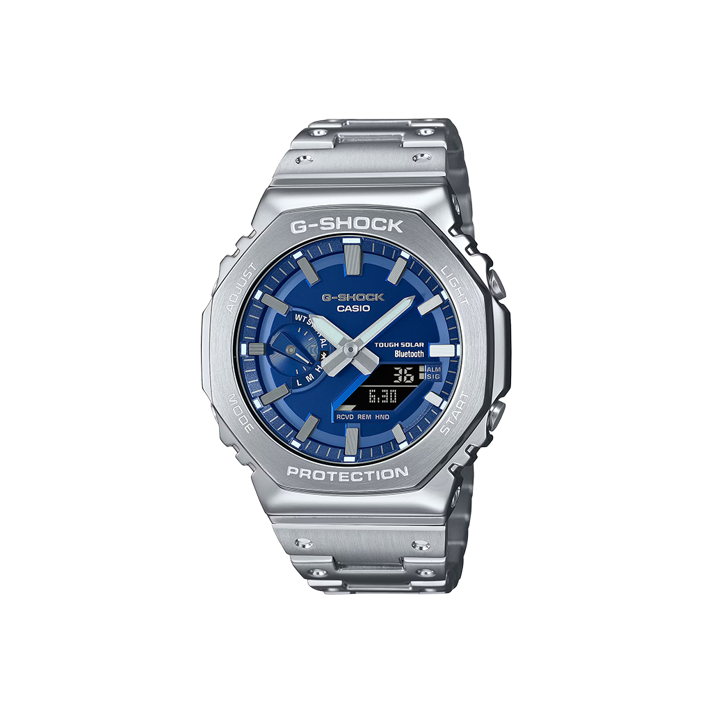 Um relógio Casio G-Shock de aço inoxidável com uma pulseira e caixa prateadas. O mostrador é azul e possui displays digital e analógico mostrando a hora. O relógio tem vários botões nas laterais, um display de dia na parte superior e vários indicadores para alarme, sinal e vida útil da bateria. As palavras “Shock Resist” indicam sua durabilidade, e “Water Resist 20 BAR” sugere uma resistência significativa à água.