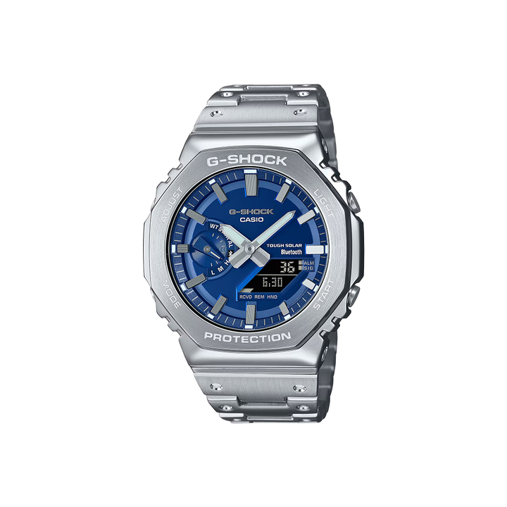 Um relógio Casio G-Shock de aço inoxidável com uma pulseira e caixa prateadas. O mostrador é azul e possui displays digital e analógico mostrando a hora. O relógio tem vários botões nas laterais, um display de dia na parte superior e vários indicadores para alarme, sinal e vida útil da bateria. As palavras “Shock Resist” indicam sua durabilidade, e “Water Resist 20 BAR” sugere uma resistência significativa à água.