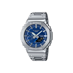 Um relógio Casio G-Shock de aço inoxidável com uma pulseira e caixa prateadas. O mostrador é azul e possui displays digital e analógico mostrando a hora. O relógio tem vários botões nas laterais, um display de dia na parte superior e vários indicadores para alarme, sinal e vida útil da bateria. As palavras “Shock Resist” indicam sua durabilidade, e “Water Resist 20 BAR” sugere uma resistência significativa à água.