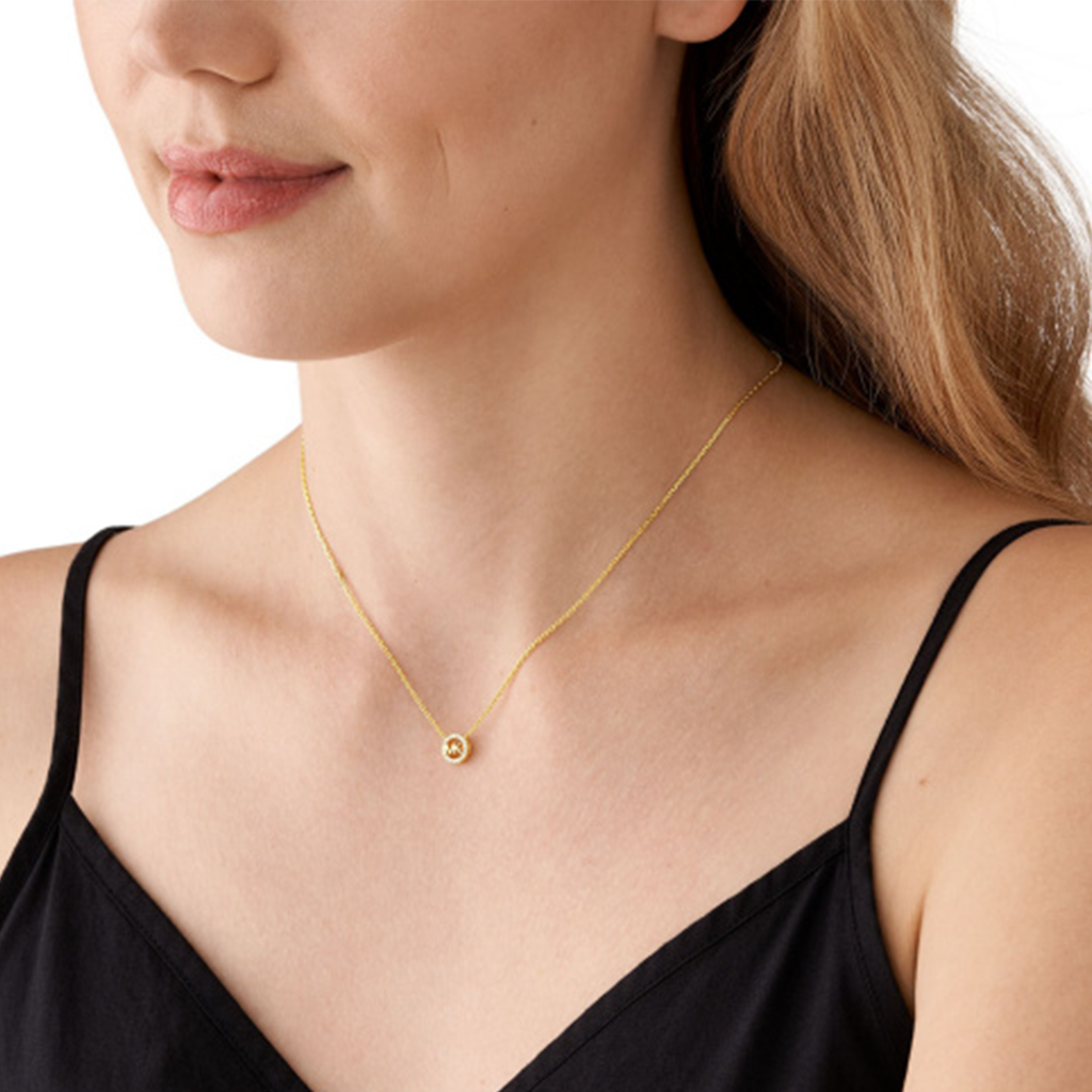 Colar delicado de prata banhada a ouro com um pequeno pingente redondo de zircónia, exibido no pescoço de uma pessoa vestindo uma blusa preta. A simplicidade do design destaca o brilho da zircónia, tornando-o um acessório elegante.