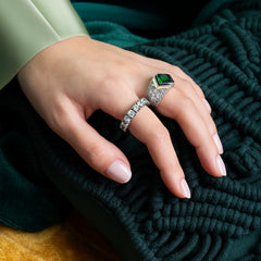 Senhora com Anel TASHI Marrakech coberto de zirónias brancas e quatro divisões (duas douradas e duas pretas) a separar a zircónia verde central. A senhora está também a usar outro anel, forrado em zircónias brancas, modelo Memória