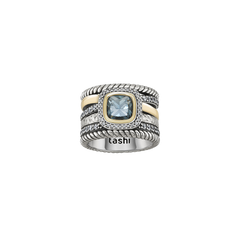 Anel TASHI London Blue grosso com seis linhas, duas cobertas em zircónias brancas, duas entrançadas, uma dourada e outra com textura rugosa. No centro está um quadrado com rebordo em zircónias brancas, seguido de detalhe dourado e no centro uma zircónia azul