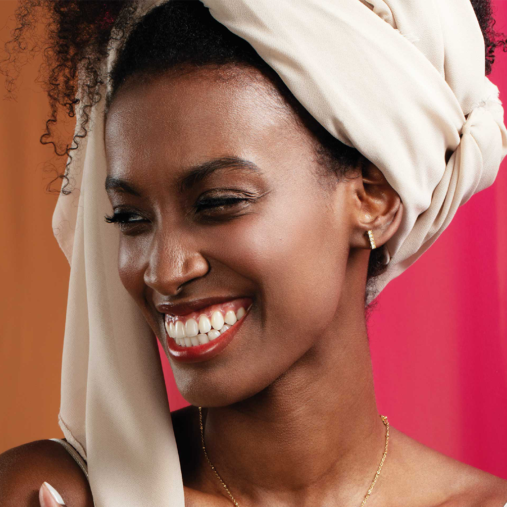 Imagem de mulher a usar um turbante branco e um brinco é visível na orelha. O fundo consiste em duas cores distintas, rosa de um lado e um tom mais escuro, possivelmente castanho ou bordô, do outro lado.