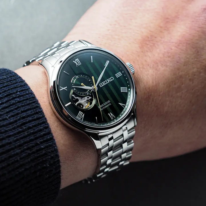 Pulso homem com Relógio Seiko Presage Japanese Garden 41.8mm de pulseira e caixa prateadas, e mostrador dourados com indicação de dia da semana e mês