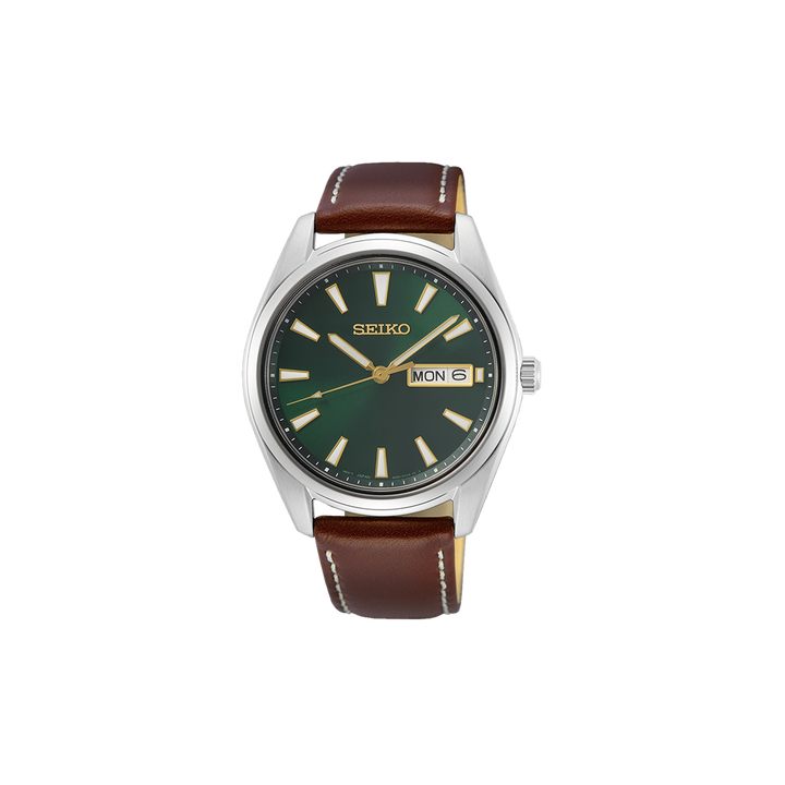 Relógio Seiko com caixa de aço inoxidável e mostrador verde escuro. O relógio possui um visor de dia e data na posição das 3 horas, com ponteiros e marcadores prateados. A pulseira é de couro bovino marrom com costura visível e fecho de fivela, combinando funcionalidade e elegância clássica.