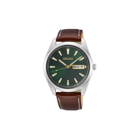 Relógio Seiko com caixa de aço inoxidável e mostrador verde escuro. O relógio possui um visor de dia e data na posição das 3 horas, com ponteiros e marcadores prateados. A pulseira é de couro bovino marrom com costura visível e fecho de fivela, combinando funcionalidade e elegância clássica.