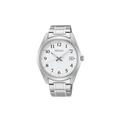 Um relógio de pulso Seiko de aço inoxidável com mostrador branco e algarismos arábicos pretos para cada hora. O relógio possui três ponteiros - dois pretos e um dourado - indicando as horas, minutos e segundos. Há um visor de data na posição das 3 horas. A caixa e a pulseira do relógio são de aço inoxidável polido, refletindo a luz em sua superfície.