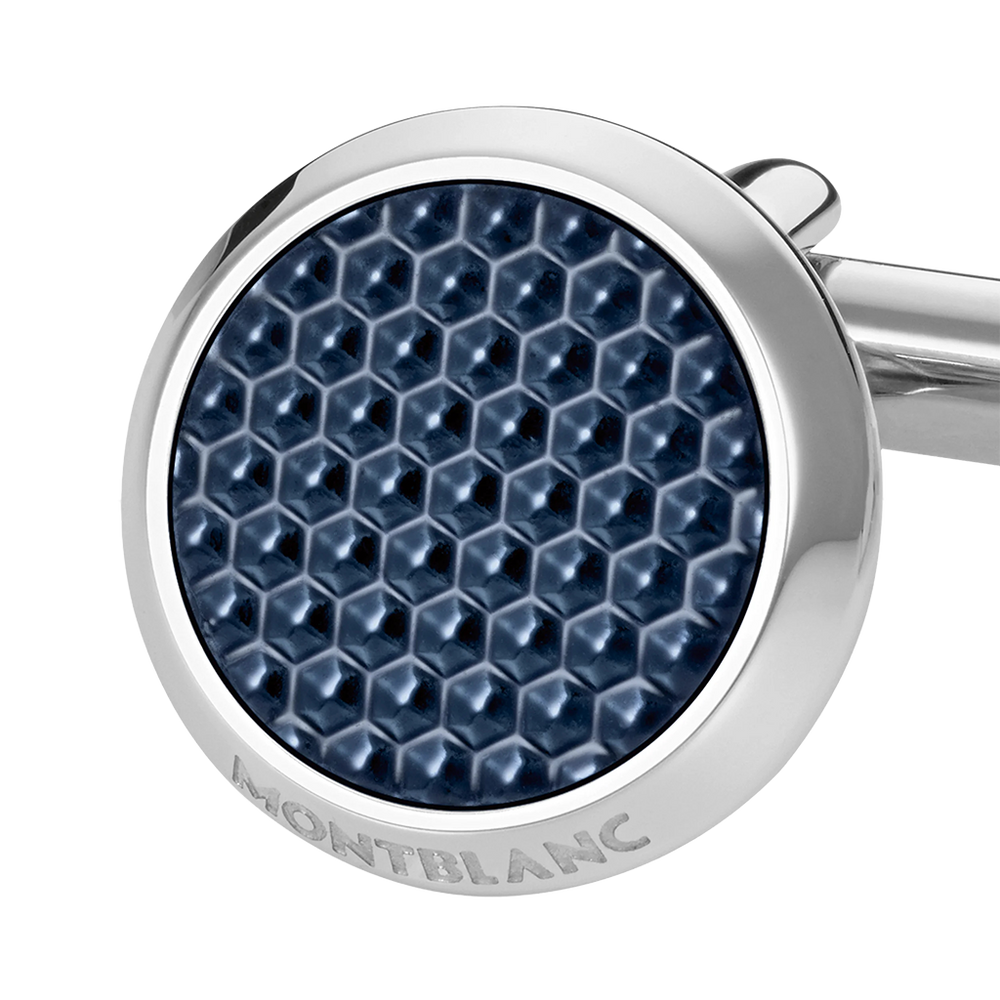 Imagem em close-up de um botão de punho redondo e prateado com laca de pedra azul. O botão de punho apresenta um padrão hexagonal detalhado na laca, dando-lhe uma aparência texturizada. O nome da marca ‘MONTBLANC’ está gravado na borda de metal que circunda a pedra azul. O fundo é branco, destacando o design e a cor do botão de punho