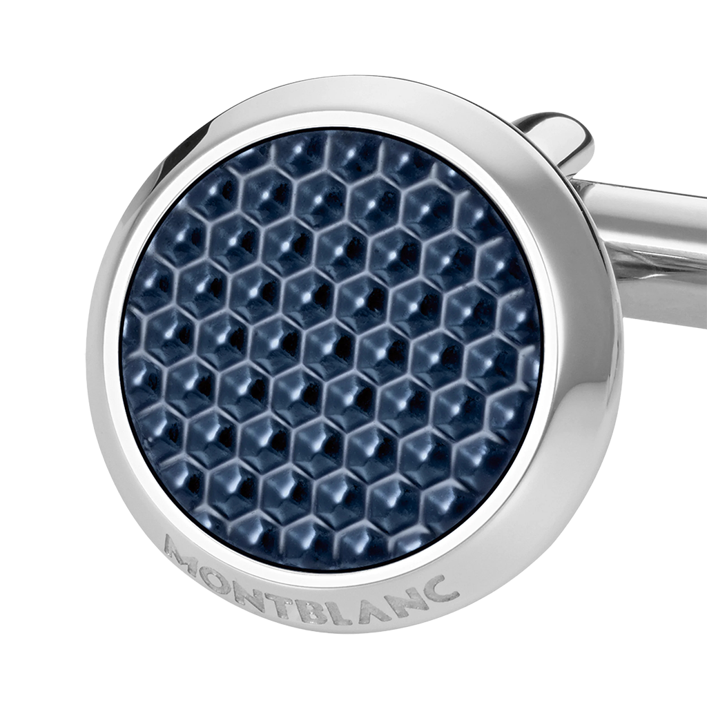Imagem em close-up de um botão de punho redondo e prateado com laca de pedra azul. O botão de punho apresenta um padrão hexagonal detalhado na laca, dando-lhe uma aparência texturizada. O nome da marca ‘MONTBLANC’ está gravado na borda de metal que circunda a pedra azul. O fundo é branco, destacando o design e a cor do botão de punho