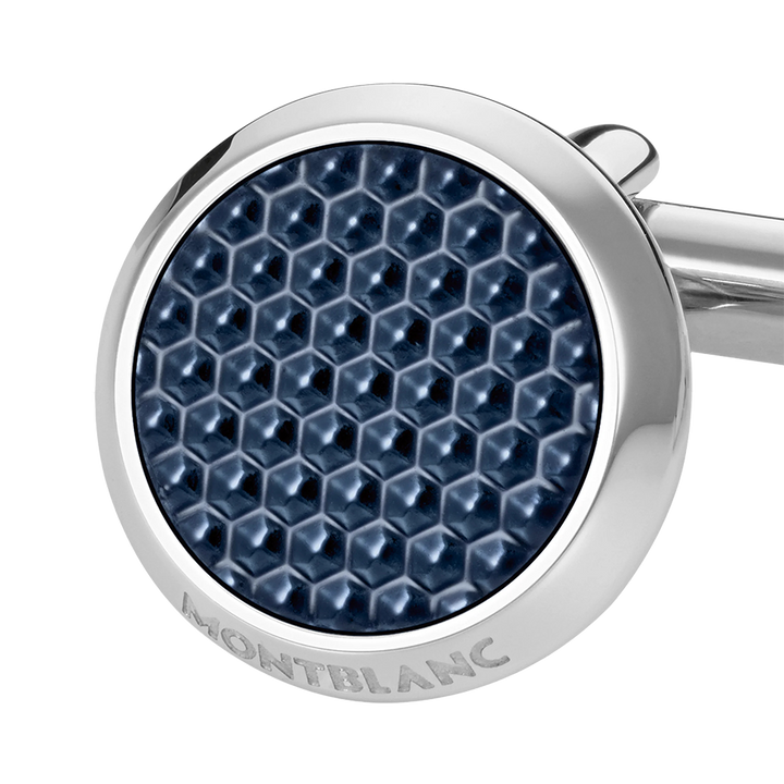 Imagem em close-up de um botão de punho redondo e prateado com laca de pedra azul. O botão de punho apresenta um padrão hexagonal detalhado na laca, dando-lhe uma aparência texturizada. O nome da marca ‘MONTBLANC’ está gravado na borda de metal que circunda a pedra azul. O fundo é branco, destacando o design e a cor do botão de punho