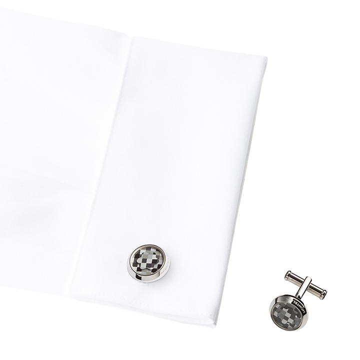 A imagem mostra uma camisa social branca dobrada com um par de botões de punho ao lado. Os botões de punho têm um padrão quadriculado preto e branco. 