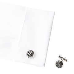 A imagem mostra uma camisa social branca dobrada com um par de botões de punho ao lado. Os botões de punho têm um padrão quadriculado preto e branco. 