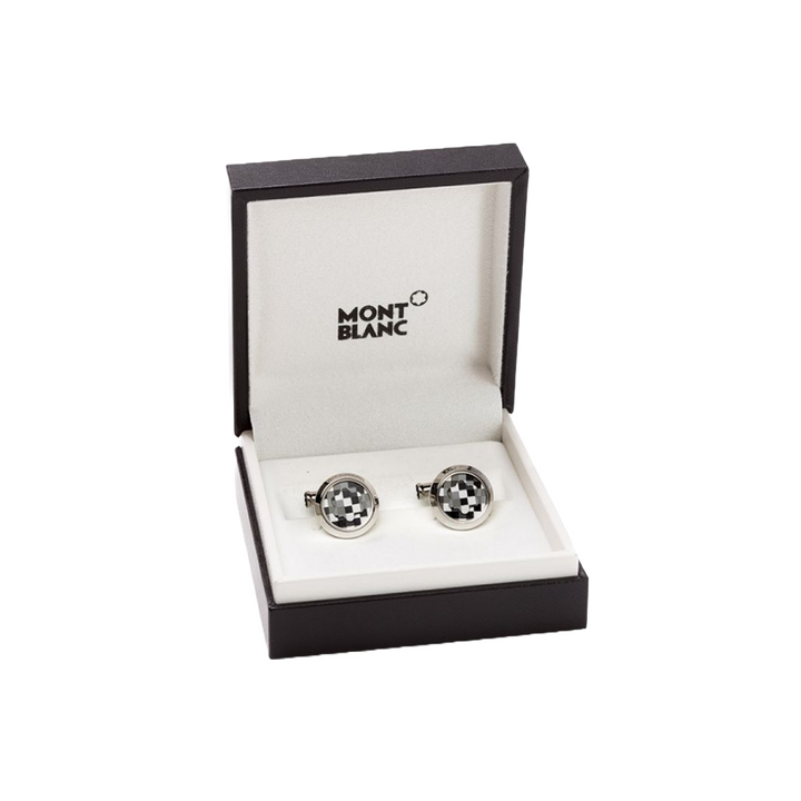 Uma caixa aberta da marca Montblanc contendo um par de botões de punho elegantes. Os botões de punho têm um design circular distinto com um padrão preto e branco contrastante que os destaca. Eles estão colocados nos slots dedicados dentro da caixa, que é marcada com ‘MONTBLANC’ na parte superior do interior. A apresentação em tal embalagem sugere que estes são acessórios de alta qualidade, possivelmente destinados a trajes formais ou como um presente de luxo.