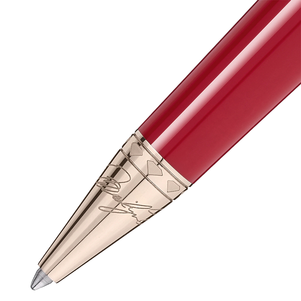 Imagem em close-up de uma esferográfica de resina com um acabamento brilhante vermelho. A caneta tem uma ponta e clipe metálicos na cor dourada, apresentando detalhes e gravações intrincados nos componentes metálicos. O design sugere elegância e uma estética clássica.