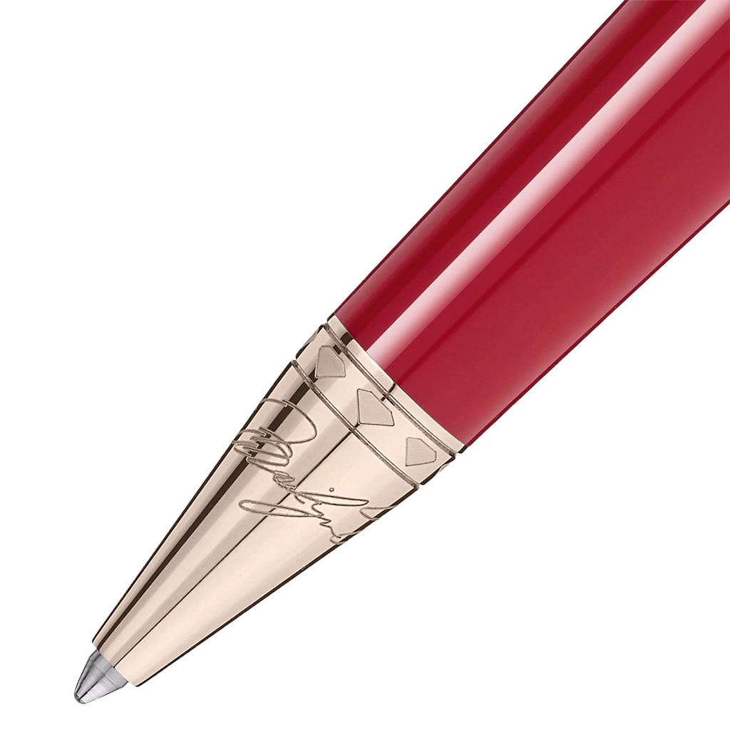 Imagem em close-up de uma esferográfica de resina com um acabamento brilhante vermelho. A caneta tem uma ponta e clipe metálicos na cor dourada, apresentando detalhes e gravações intrincados nos componentes metálicos. O design sugere elegância e uma estética clássica.