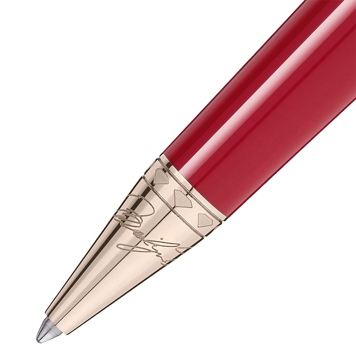 Imagem em close-up de uma esferográfica de resina com um acabamento brilhante vermelho. A caneta tem uma ponta e clipe metálicos na cor dourada, apresentando detalhes e gravações intrincados nos componentes metálicos. O design sugere elegância e uma estética clássica.