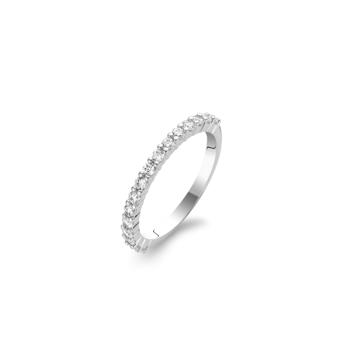 Imagem de um anel em aço banhado a platina, adornado com várias pedras de zircónia de corte redondo, dispostas em uma única fileira ao longo da metade superior da banda. O anel é exibido contra um fundo branco simples, destacando seu acabamento lustroso e a clareza cintilante das gemas.