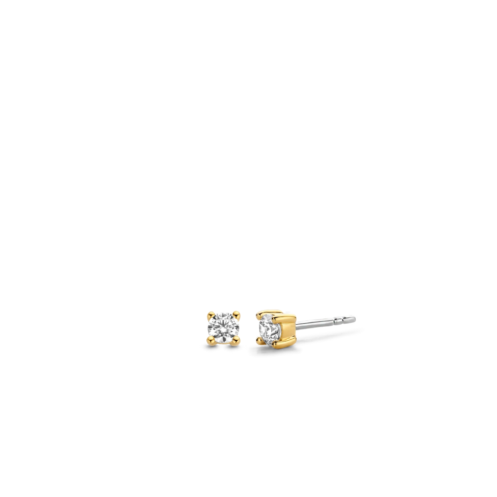 Um par de brincos Ti Sento de prata banhados a ouro, apresentando um design simples, mas elegante. Cada brinco tem uma pedra de zircónia proeminente fixada no centro, segura por quatro garras banhadas a ouro que proporcionam um ajuste seguro e realçam o brilho da pedra. Os brincos têm um fecho de tarraxa, adequado para orelhas furadas. O contraste entre a prata e o banho de ouro adiciona ao apelo luxuoso destes acessórios sofisticados