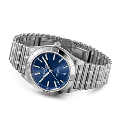 Um relógio de pulso em aço inoxidável com uma pulseira de elos. O relógio tem um mostrador azul com ponteiros e marcadores de hora em tom prateado. Há uma exibição de data na posição das 3 horas, e o nome da marca é visível abaixo do marcador das 12 horas. A coroa do relógio está posicionada no lado direito da caixa, e parece ter um acabamento polido.