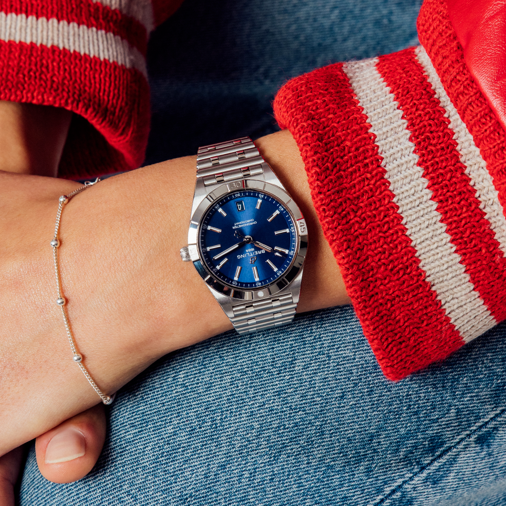 Relógio Breitling Chronomat em aço inoxidável com acabamento polido. O relógio tem uma caixa redonda com o logotipo da Breitling e ‘Certifie Chronometre’ inscritos no centro. A coroa é visível no lado direito da caixa, indicando sua função para ajuste de tempo. A pulseira apresenta elos largos com um fecho de implantação.