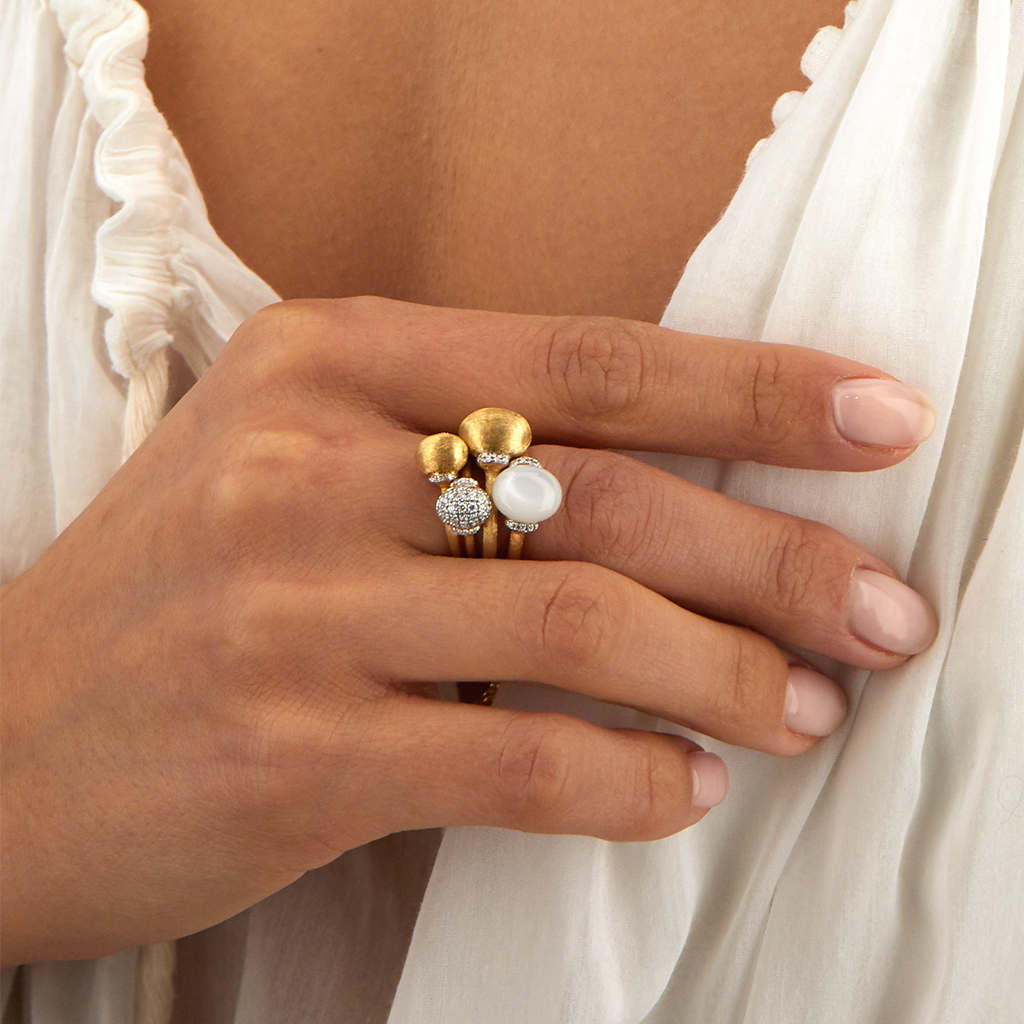 imagem de senhora a segurar camisola em que mistura no dedo do meio vários anéis de ouro e diamantes com o do anel Amuleti White Desert com uma pedra da lua com aro em ouro 18kt e rodeado de diamantes