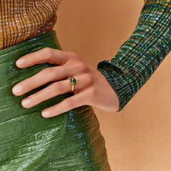 imagem em close up de mão de mulher com verniz branco com anel de turmalina verde. a mão está pousada numa anca de uma mulher com uma saia verde