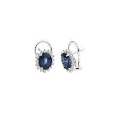 Um par de brincos de ouro branco apresentando safiras de corte oval cercadas por um halo de pequenos diamantes redondos. Os brincos têm um fecho de alavanca e são colocados contra um fundo branco simples, destacando seu design elegante e o contraste entre o azul profundo das safiras e o brilho brilhante dos diamantes.
