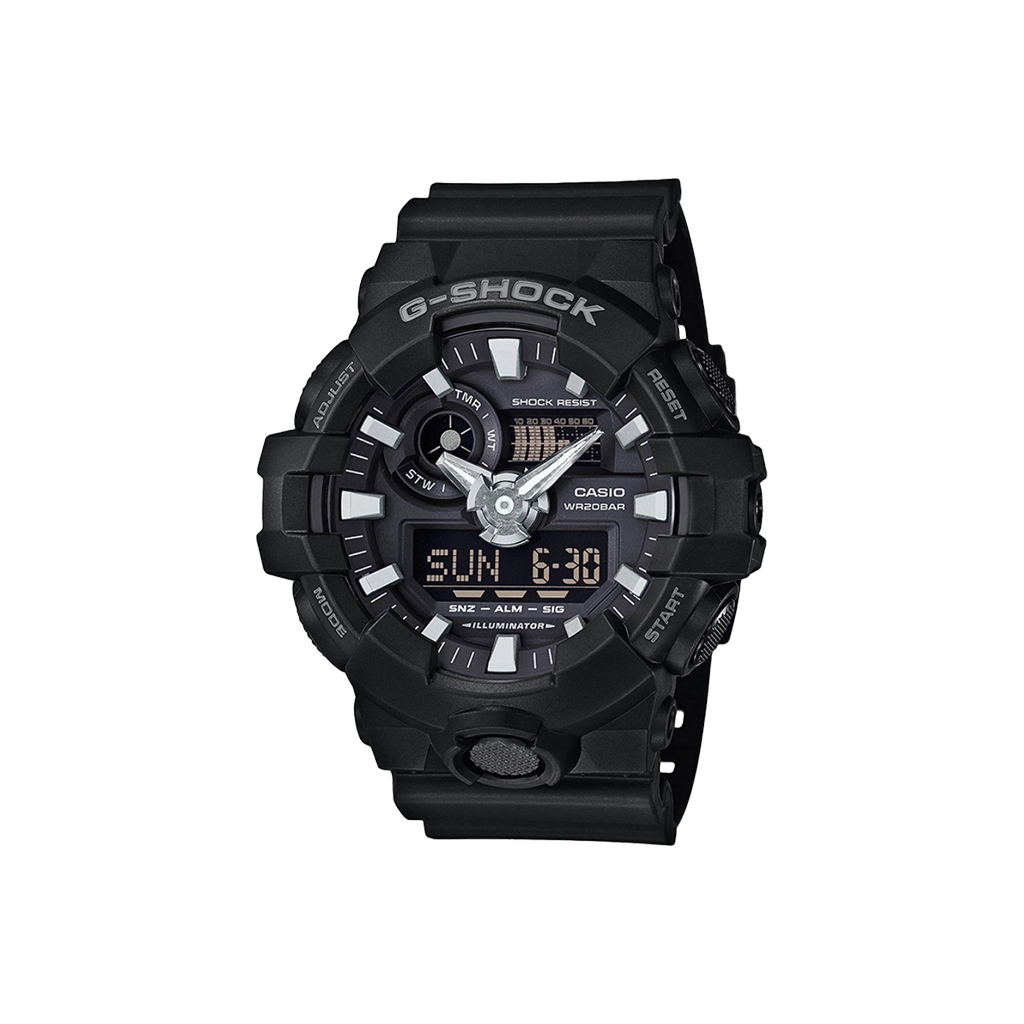 Relógio Casio G-Shock com bracelete de resina preta. O mostrador combina displays analógicos e digitais, com ponteiros prateados e marcadores de hora sobre um fundo preto. O mostrador digital exibe a hora em formato numérico. O bisel é marcado com indicadores de minutos e a inscrição “SHOCK RESIST”. Funções adicionais incluem exibição de dia e data, além de configurações de alarme visíveis no mostrador.