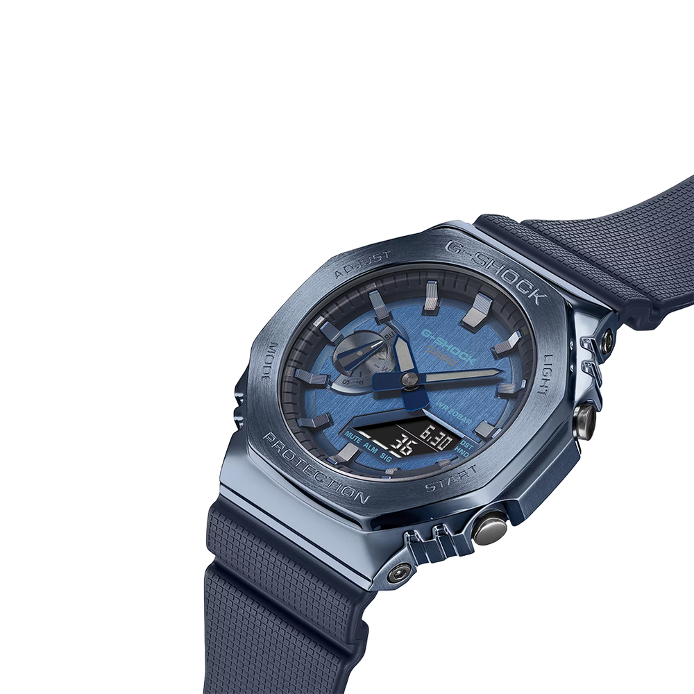 Relógio de pulso de resina com mostrador transparente azul e pulseira azul correspondente. O design é robusto, com parafusos visíveis no aro, e a marca ‘G-SHOCK’ está destacada na parte superior do mostrador. Os ponteiros são metálicos e há várias marcações e textos no mostrador indicando recursos de medição de tempo. O fundo é branco, destacando os detalhes do relógio.