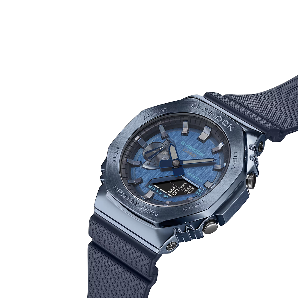 Relógio de pulso de resina com mostrador transparente azul e pulseira azul correspondente. O design é robusto, com parafusos visíveis no aro, e a marca ‘G-SHOCK’ está destacada na parte superior do mostrador. Os ponteiros são metálicos e há várias marcações e textos no mostrador indicando recursos de medição de tempo. O fundo é branco, destacando os detalhes do relógio.
