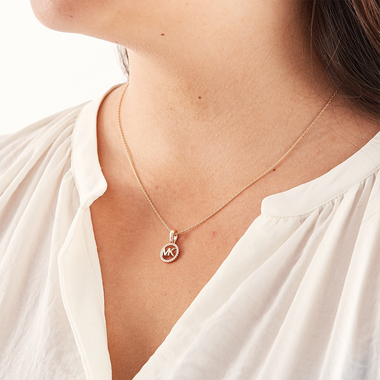 Colar de prata banhada a ouro com um pendente apresentando as iniciais ‘MK’ cravejadas de zircónias, usado por uma pessoa vestindo uma blusa branca.