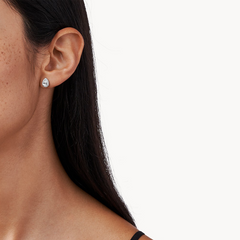 Vista lateral de uma pessoa com cabelo longo e escuro, ombro com uma alça preta visível que pode ser parte da roupa, e um fundo branco simples